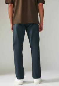 Pantalones azul marino ajustados, confeccionados con una tela ligera, con una textura suave y un corte regular, combinados con zapatillas blancas.