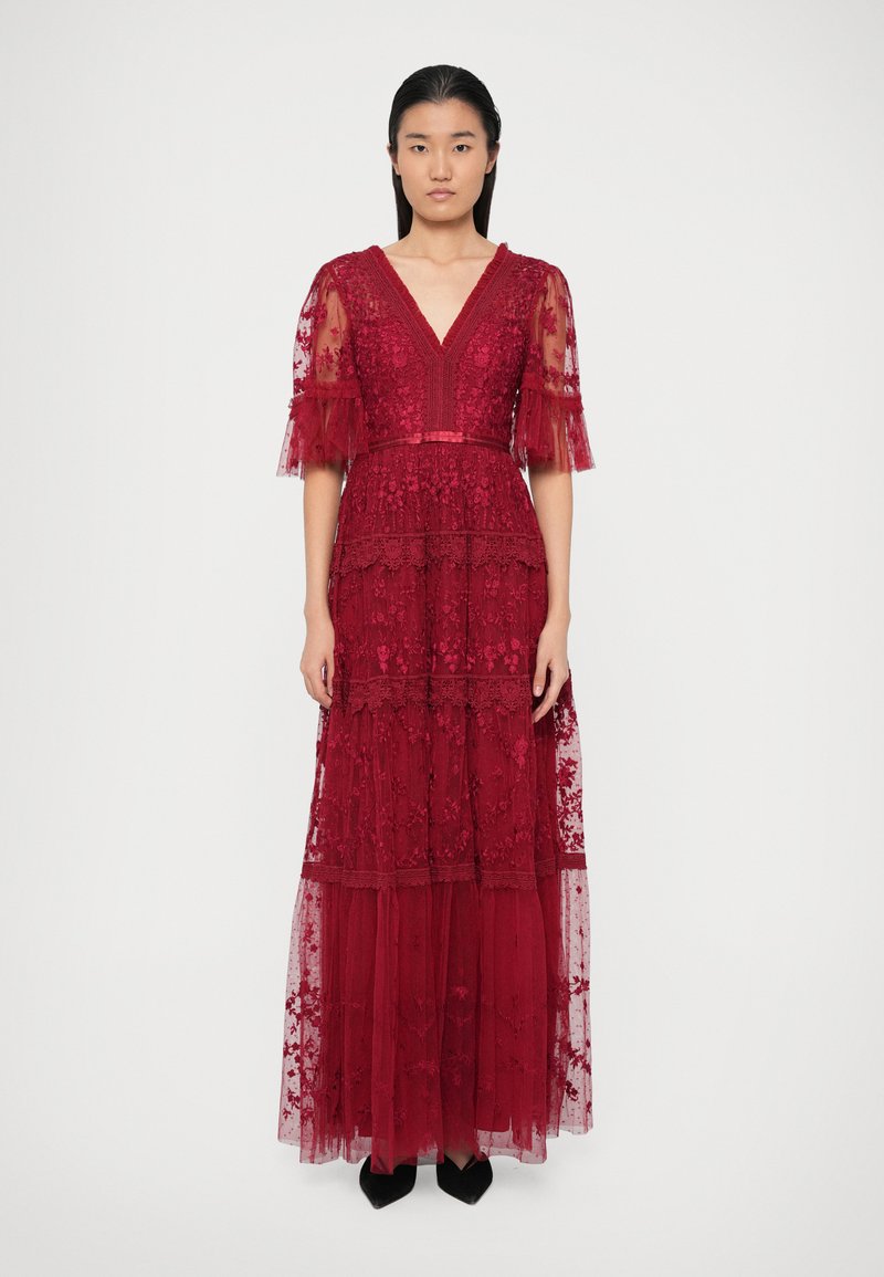 Punane pitskleit lühikeste, laienevate varrukatega, sügava V-dekolteega, kihilise seelikuga, keeruka tikandiga ja figuretuvööga. Mustad kingad lõpetavad välimuse.