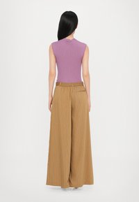 Purple ribbed sleeveless top paired with high-waisted, wide-leg brown striped trousers. Soft texture and loose fit, accentuating design details.