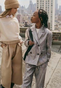 Due bambini stanno su un tetto. Uno indossa una felpa color crema con strass, mentre l'altro è in un elegante completo argento doppiopetto.