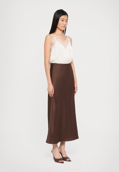 Silk camisole in white with lace detailing, paired with a brown satin maxi skirt. Model wears brown open-toe heels.