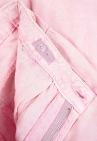 Jasnoróżowa tkanina dżinsowa z widokiem od wewnątrz, z przeszytymi krawędziami, zapięciem na guzik oraz zamykaną kieszenią. Miękka, teksturowana powierzchnia.