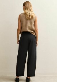Beżowy, bezrękawnik z dzianiny, czarne spodnie o szerokich nogawkach oraz czarne buty. Gładka tekstura, neutralne kolory, minimalistyczny design i luźny krój.