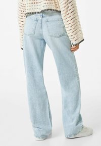 Ljusblå vida jeans med en blekt struktur, med två bakfickor och en rå kant vid fållen, kombinerat med en stickad topp.