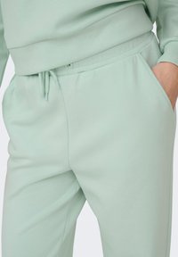 Svetlo meta zelene hlače jogger iz mehke tkanine, z elastičnim pasom z vrvico in bočnimi žepi za priročnost.