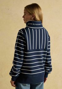 Tumesinine triibuline pullover kõrge kraega, valgete horisontaalsete triipudega, tikitud "JOULES" detailiga ning soonikkoes varrukate ja alumise äärega.