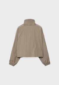 Veste marron clair à manches longues avec col montant, poignets élastiques et bandes blanches le long des épaules, vue de dos sur un fond uni.