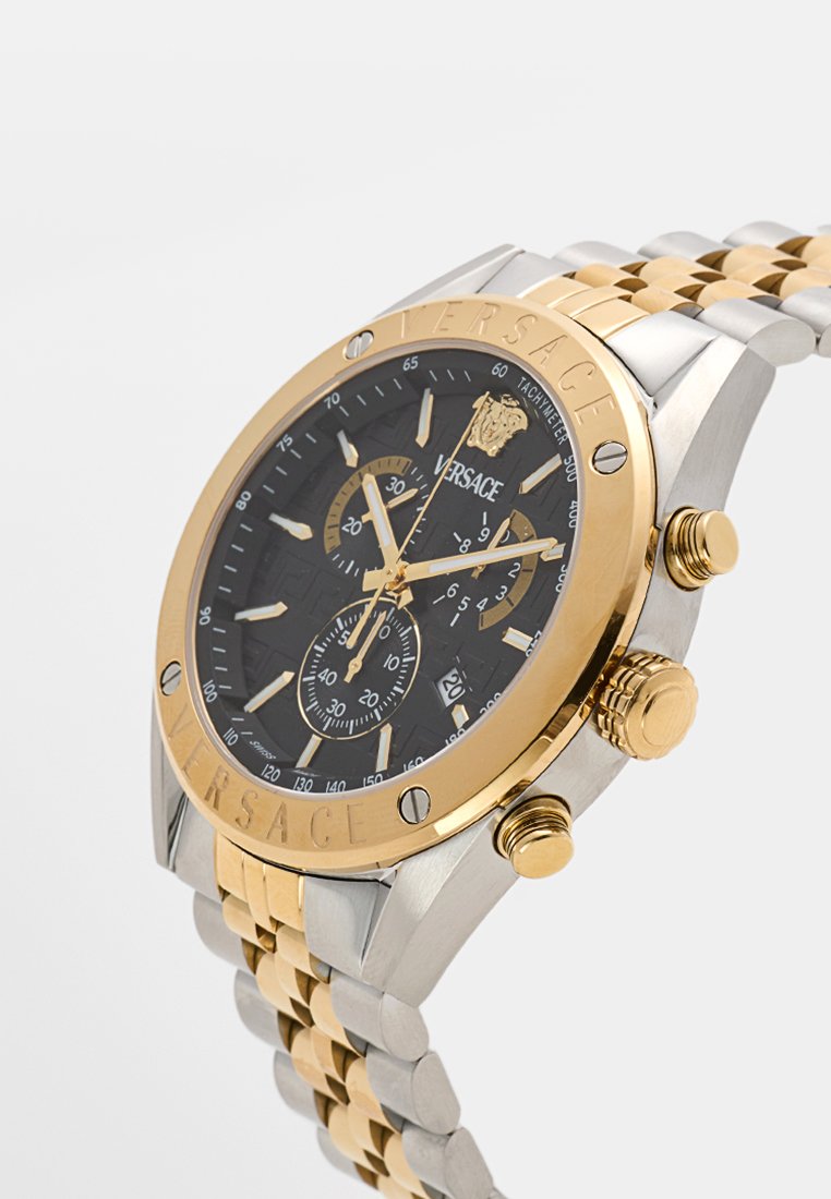 Montre-bracelet en acier inoxydable doré et argenté avec un cadran noir, des fonctionnalités de chronographe, des accents dorés et un bracelet à motif. Marque Versace visible.