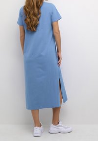 Sininen, lyhythihainen, polven pituinen mekko, jossa on sivuhalkiot ja joka on valmistettu pehmeästä kankaasta. Yhdistetty valkoisiin lenkkitossuihin. Minimalistinen muotoilu.