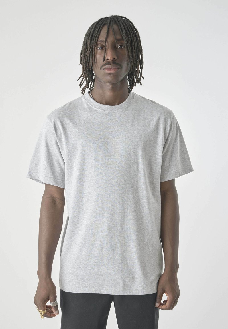 Helles graues, kurzärmliges Jersey-T-Shirt mit rundem Ausschnitt; hat einen lässigen Schnitt und eine weiche Textur. Wird mit schwarzen Hosen getragen.