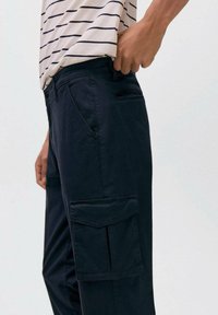 Mornarsko cargo hlače iz bombaža z gladko teksturo, z bočnimi žepi in ravnim krojem, v kombinaciji z črtasto kratkimi rokavi majico.