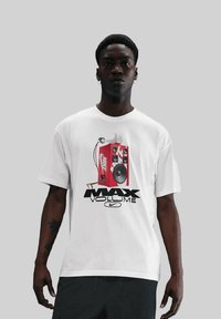 Hvid bomulds T-shirt med et rødt højttaler grafik og teksten "MAX VOLUME" samt Nike-logo. Korte ærmer og afslappet pasform.