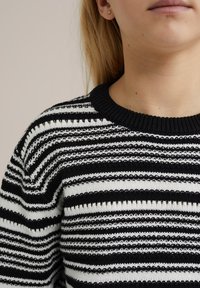 Svart och vitrandig tröja med ribbad halsringning och varierande horisontella mönster i en stickad textur.