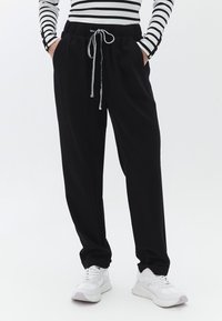 Sorte joggerbukser med elastisk talje og snor, der har sidelommer og en afslappet pasform, parret med hvide sneakers.