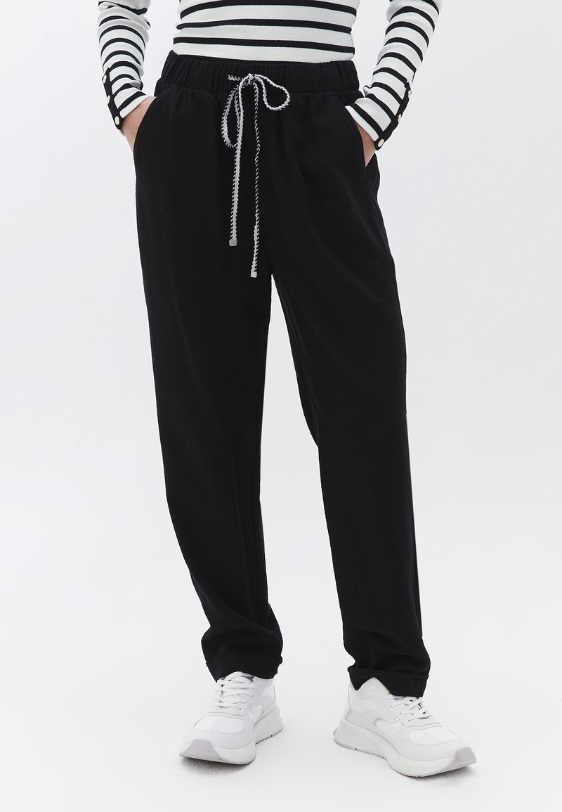 Sorte joggerbukser med elastisk talje og snor, der har sidelommer og en afslappet pasform, parret med hvide sneakers.