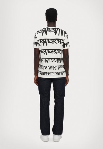 Weißes T-Shirt mit schwarzem abstraktem Textmuster, kurzen Ärmeln und Rundhalsausschnitt; kombiniert mit dunklen Jeans und weißen Turnschuhen.