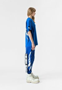 Camiseta azul de gran tamaño y joggers a juego, con patrones de alas, detalles de etiqueta y botas de plataforma blancas gruesas. Textura suave.