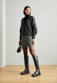 Pilkas megztinis, juoda golfas, žalia odinė mini sijonas ir juodi ilgaauliukai. Ypatinasi sklandžiais audiniais ir subtiliais akcentais.