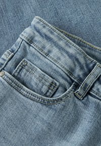 Jeans in denim blu chiaro con vita visibile, passanti per cintura e taschino piccolo. Il tessuto presenta una sottile texture e dettagli di scoloritura.