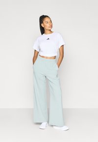 Vit kort t-shirt med svart Adidas-logotyp, kombinerad med ljus mintgröna vida byxor. Outfiten har en avslappnad passform och elastisk midjeband.