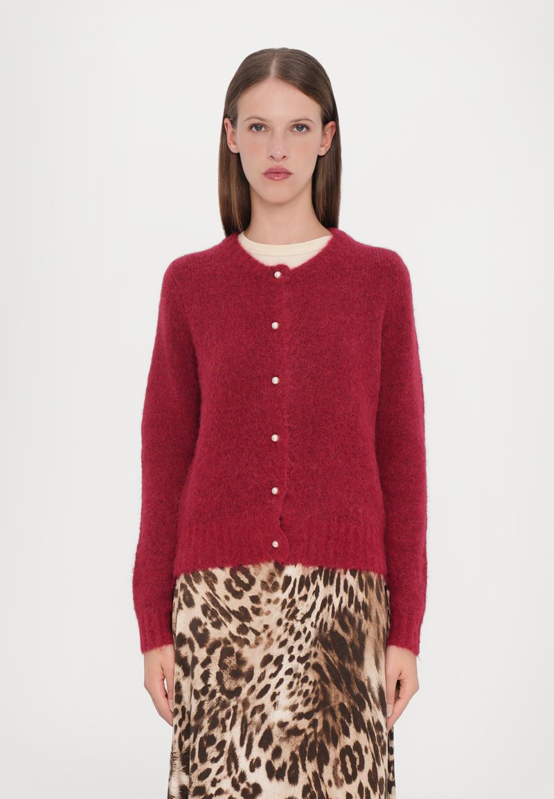 Cardigan rosso e morbido con scollatura rotonda e bottoni perla, abbinato a una gonna con stampa leopardata. Tessuto soffice e vestibilità casual.