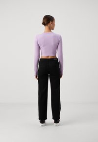 Lilac long-sleeve crop top paired with black wide-leg pants and patterned socks. Model shown from the back with a simple hairstyle.