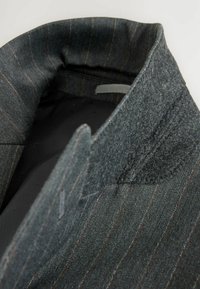 Grau gestrickte Blazerkragen aus Wollmischung mit feinem Nadelstreifenmuster, der eine weiche Textur und einen kontrastierenden Filz-Akzent am Hals aufweist.