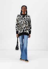 Suéter de estampado de leopardo en crema, negro y gris, con un cuello acanalado negro. Combinado con jeans de campana azules y un bolso de hombro negro.