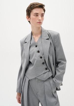 Grau maßgeschneideter Anzug mit einem strukturierten Blazer, der auffällige Revers und fünf schwarze Knöpfe hat, kombiniert mit einer passenden gefalteten Hose.