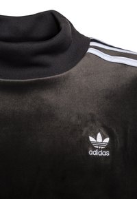 Svart velourtröja med hög krage, med vita accentstreck och en broderad Adidas-logotyp på vänstra sidan.