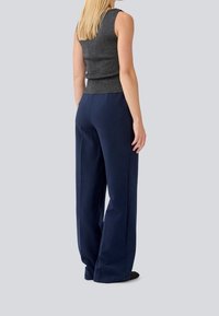 Grå ærmeløs top med en struktureret overflade, parret med navy bukser med bred ben, der har høj talje og en glat stof.