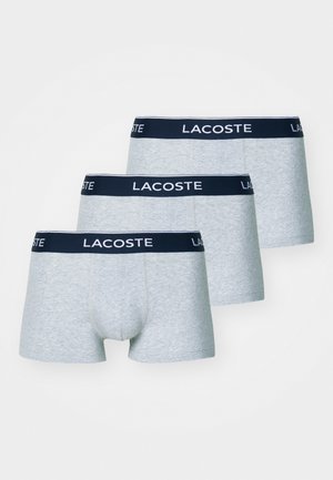 Drei Paar graue Boxershorts mit einem marineblauen Bund, auf dem das "LACOSTE"-Logo in Weiß prangt. Weicher Stoff und enganliegendes Design.
