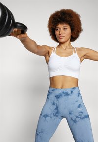 Crop top de sport blanc avec des bretelles fines, associé à un legging taille haute bleu marbré avec une taille élastique et un détail de logo.