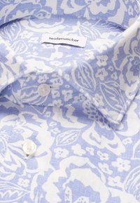 Col de chemise bleu clair et blanc à motif floral avec boutons blancs et étiquette de marque "seidensticker" visible.