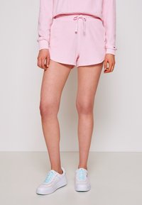 Felpa rosa chiaro e pantaloni corti abbinati con vita elastica e lacci. Indossati con sneaker bianche con lacci azzurri.