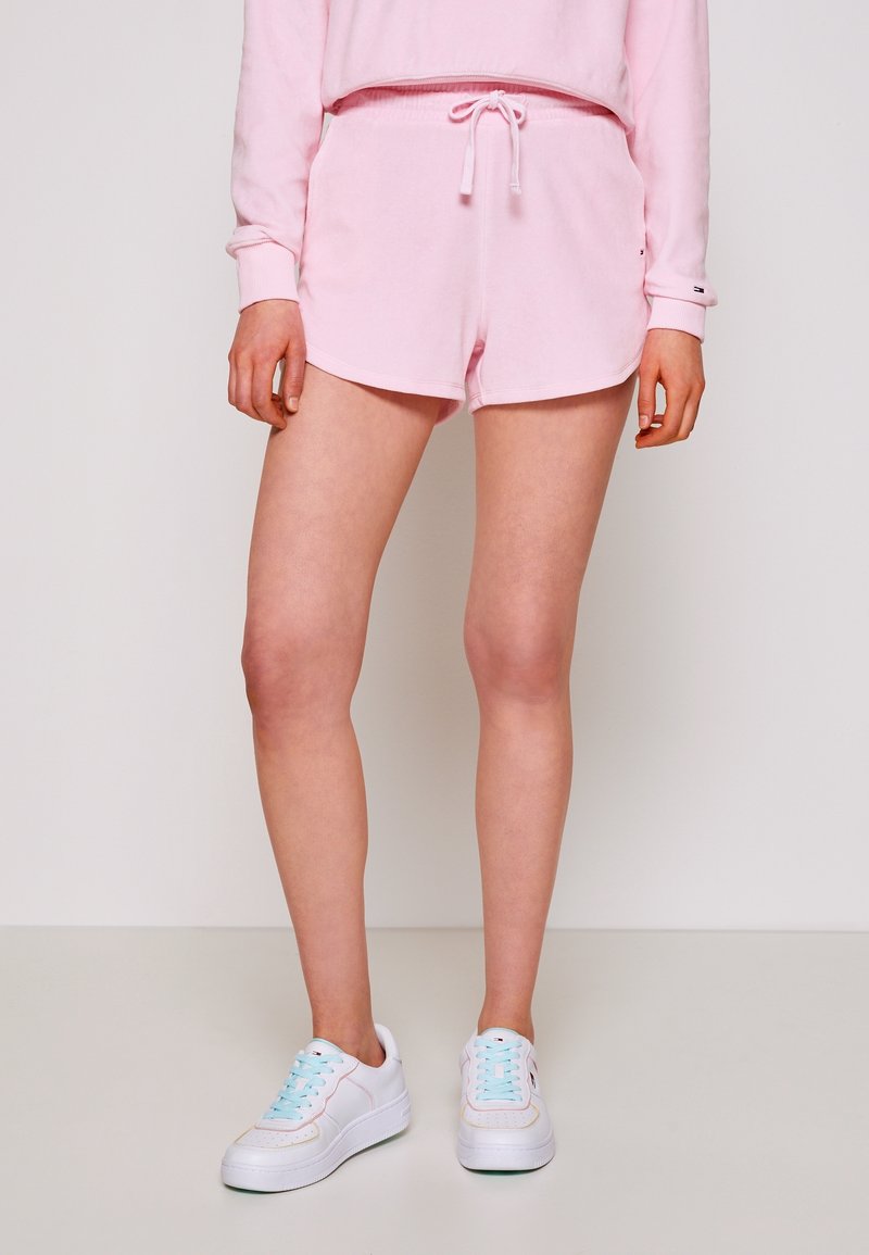 Felpa rosa chiaro e pantaloni corti abbinati con vita elastica e lacci. Indossati con sneaker bianche con lacci azzurri.