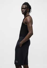 Μαύρο αμάνικο τοπ και μαύρο αθλητικό σορτς με πλαϊνές τσέπες· τα σορτς διαθέτουν κεντημένο λογότυπο· απαλό, ελαστικό ύφασμα.