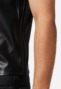 Schwarze Lederweste mit glatter Oberfläche, ausgestattet mit einem seitlichen Reißverschluss, figurbetontem Schnitt und ohne Ärmel, kombiniert mit schwarzer Jeans.