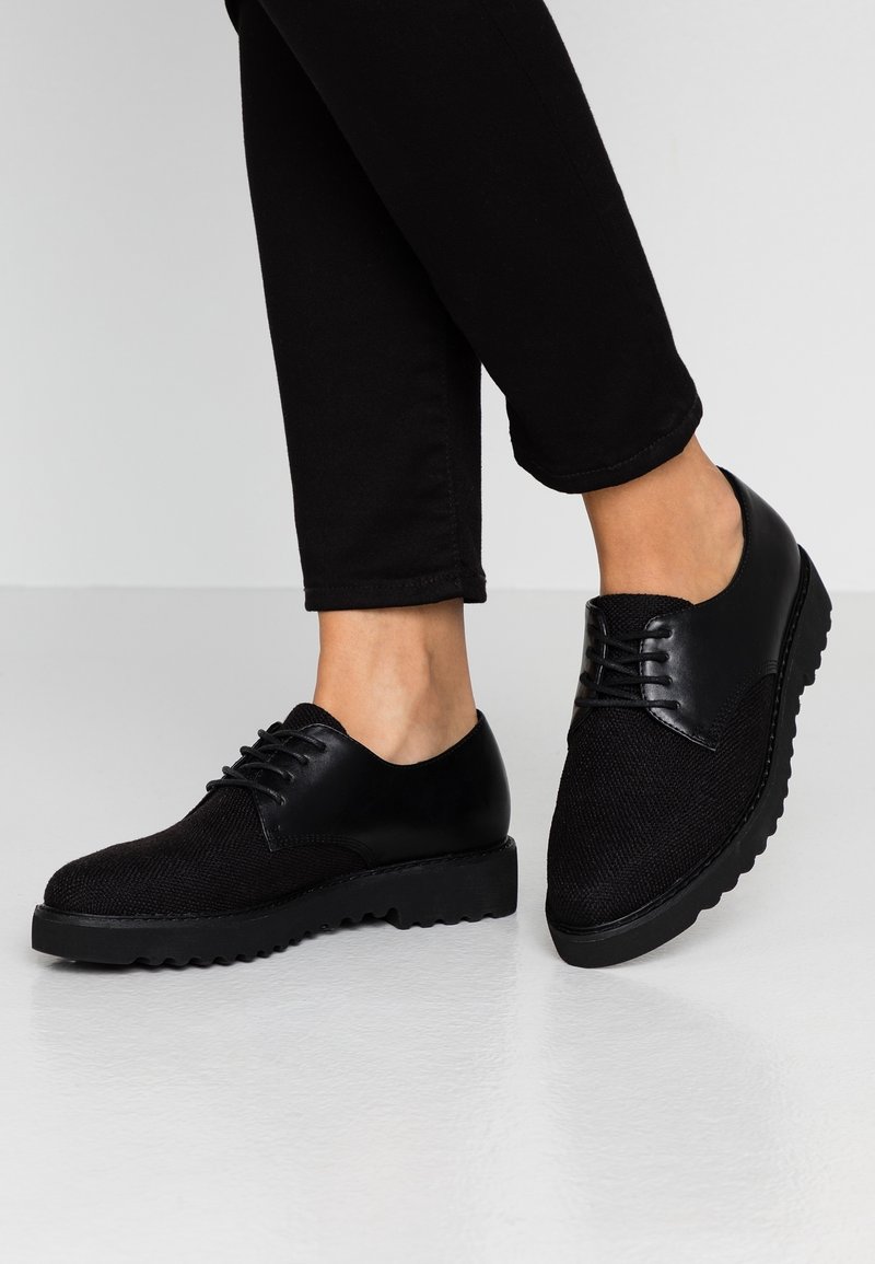 Chaussures noires à lacets avec une tige en tissu texturé, des accents en cuir lisse et une semelle en caoutchouc épaisse avec un motif en relief.