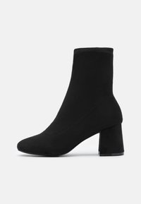 Bottines noires en matière douce, avec un bout pointu et un talon carré épais. Texture lisse sans motifs ni accessoires visibles.