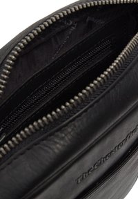 Interno di una borsa a pochette in pelle nera, con un compartimento con zip, caratterizzato da una texture liscia e un rivestimento interno nero a contrasto. Branding sottile visibile.