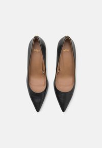 Scarpe nere in pelle con tacchi alti e punta appuntita. L'interno è marrone chiaro, con un logo dorato "BOSS" sulla soletta.