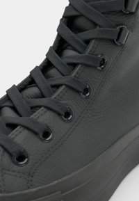 Baskets en cuir noir avec surface texturée, dotées de lacets plats noirs, d'œillets ronds et d'une semelle en caoutchouc robuste.