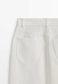 Vue arrière d'un jean en denim blanc montrant les passants de ceinture et deux poches arrière sur un fond uni.