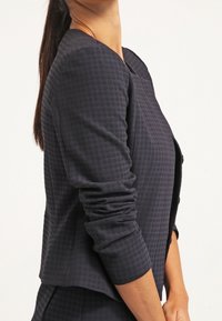 Blazer testurizzato blu navy con un motivo geometrico, caratterizzato da maniche lunghe e una silhouette strutturata. Chiusura con bottoni frontale.