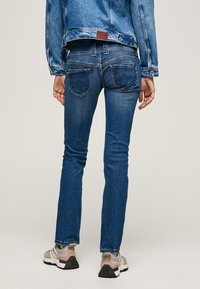 Mørkeblå denimjeans i slim fit, med fem lommer, kontrasterende sømmer og en rund midje, sammen med grå og beige sneakers.