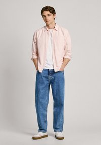 Svetloružová a biela pruhovaná košeľa s gombíkmi cez biele tričko, v kombinácii so voľnými modrými džínsy a bielymi teniskami.