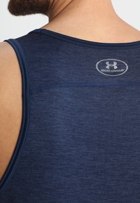 Maglietta sportiva senza maniche blu navy realizzata in tessuto texturizzato con dettagli di cucitura. Logo mostrato sulla parte superiore della schiena.