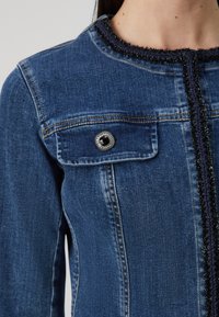 Denim jasje in donkerblauw met een ronde halslijn, versierd met een textuurafwerking en een metalen knoopdetail op de borstzak.