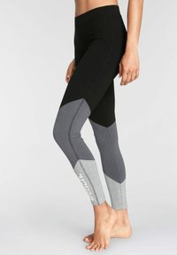 Svarta och grå leggings med en geometrisk färgblockdesign, med en melerad grå accent och en logotyp nära ankeln. Mjuk textur och åtsittande form.